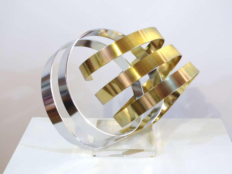 Signed ribbon sculpture by Dan Murphy, circa 1983. Gleaming anodized chrome and gold tone aluminum float effortlessly atop a solid lucite base.