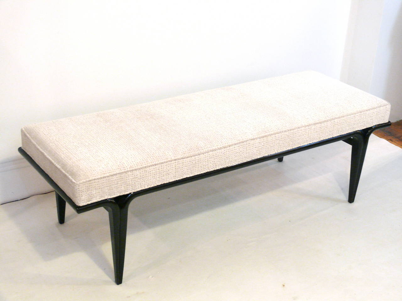 Stunning mid-century bench in the manner of T.H. Robsjohn-Gibbings with a high gloss ebonized walnut base, beautiful tapered legs, and reupholstered in a rich grid texture beige chenille.