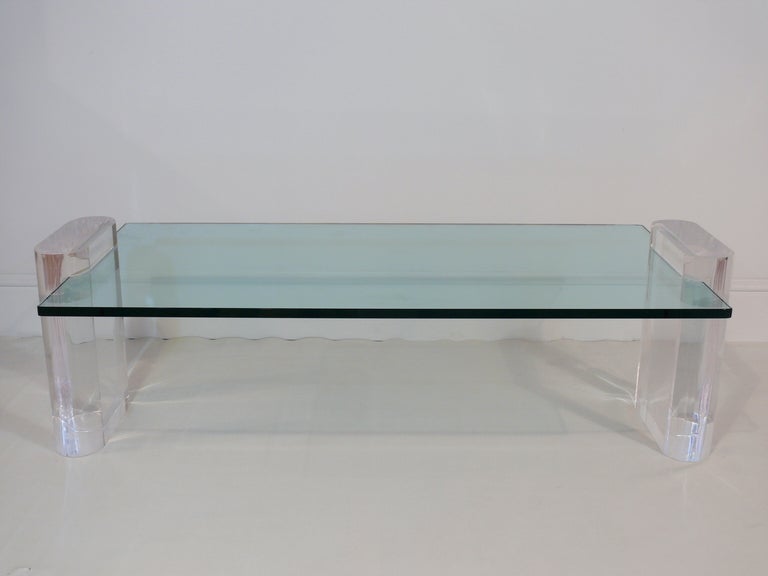 Lucite and glass coffee table in the manner of Karl Springer. Two oval shaped pieces of Lucite have a notch that holds a 3/4