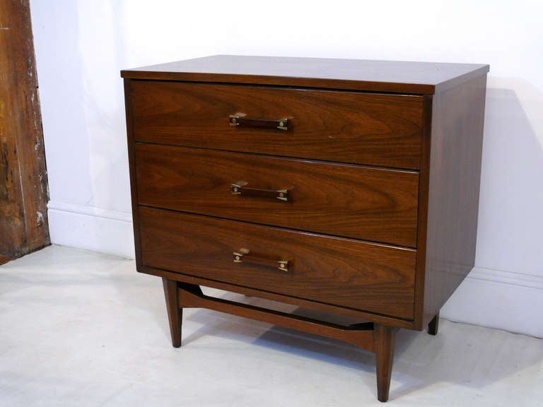 Pair of Mid-Century walnut three drawer chests with brass and wood hardware.  Chests stand on a sculptural base.