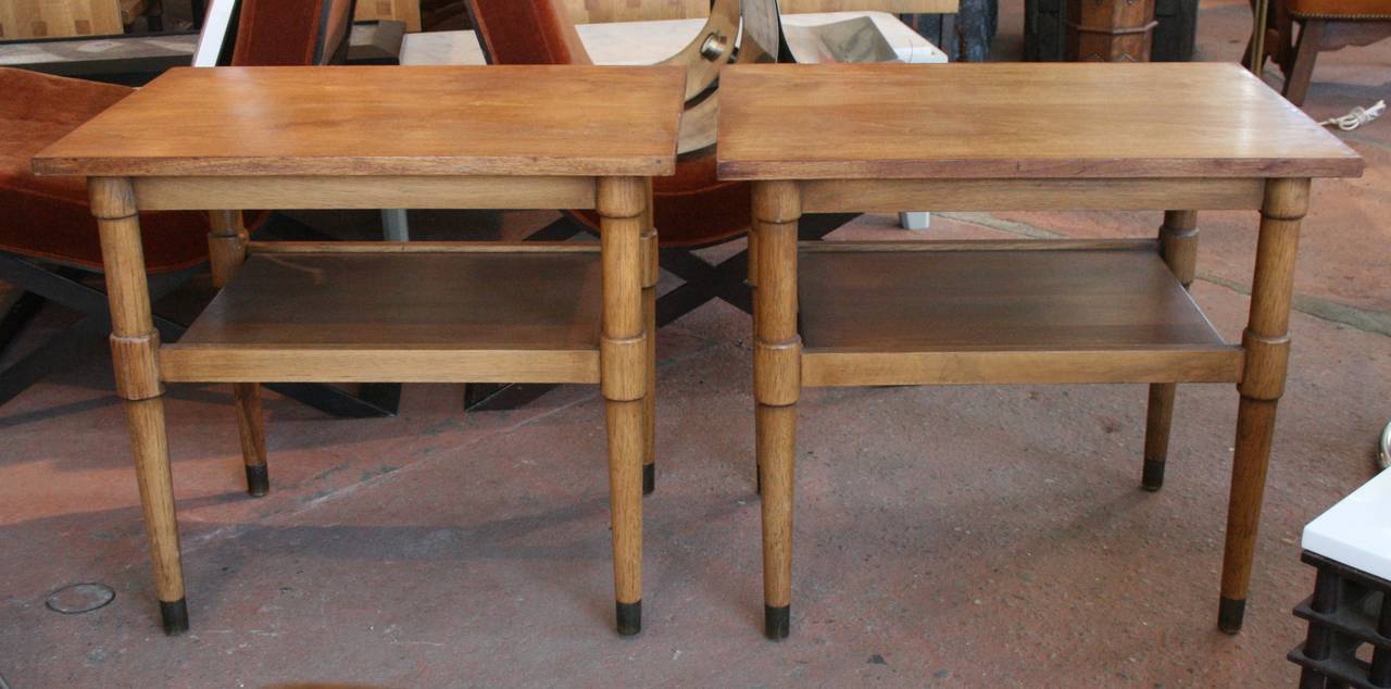 Pair of Drexel walnut end tables with lower shelf and aged brass foot caps.