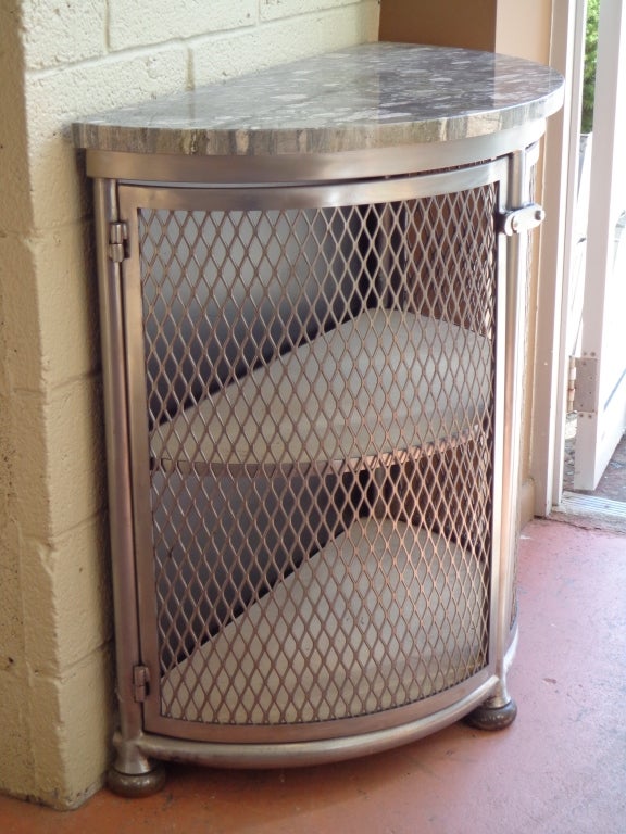 Tubular steel demilune cabinet with mesh doors, bun feet, fossiled marble top, wood shelves.