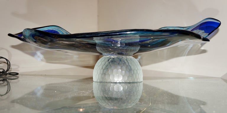 An abstract artwork obtained through the infusion in the hot glass of murrine and colored  glass rods. The large glass stands on a heavy hand hammered clear glass base. Edges are wavy enhancing the sculptural effect created by the clear and colored