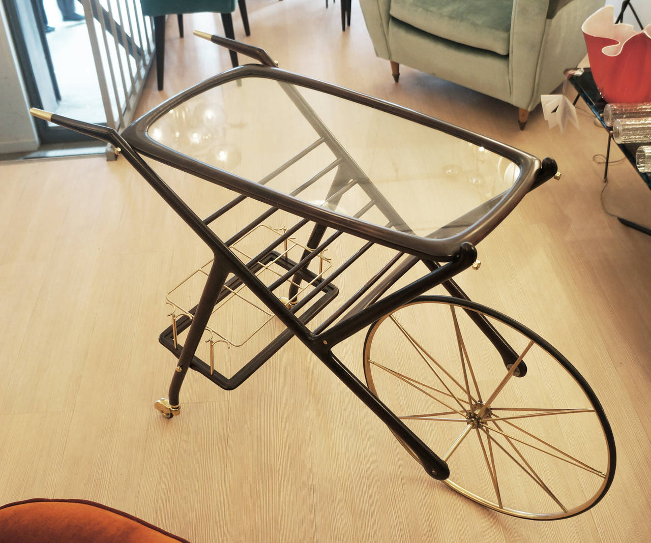 This bar cart differs tremendously from most of the others by the fact that it has one very large and two small wheels and it is also higher than most bar carts thus facilitating serving drinks. The top has a framed glass. Under the top in the