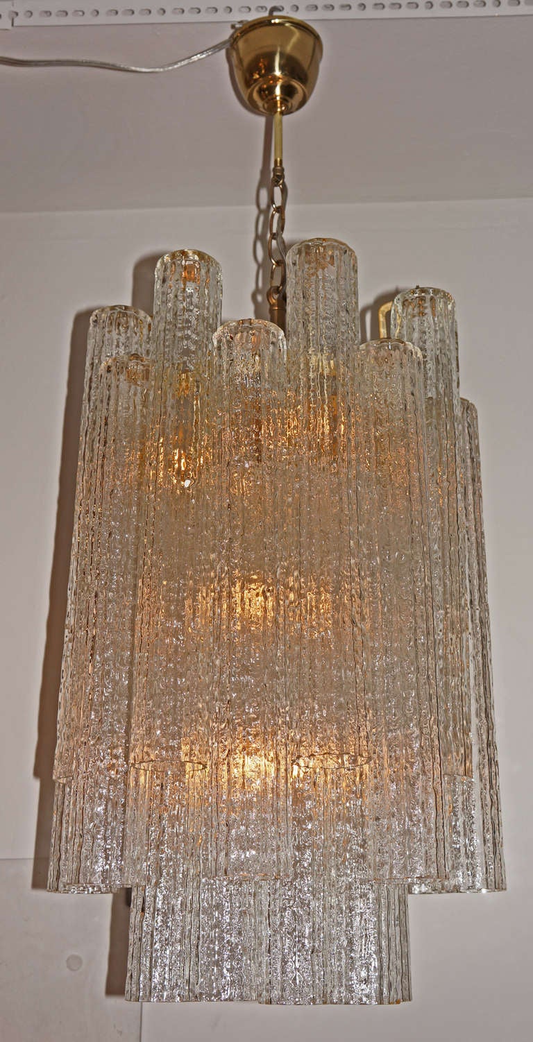 Very elegant Murano chandelier made with elongated hand blown clear glass tubes with an irregular and ribbed surface that hides completely the lamp bulbs. Glasses hang from an off white metal structure connected to the ceiling by brass chain and