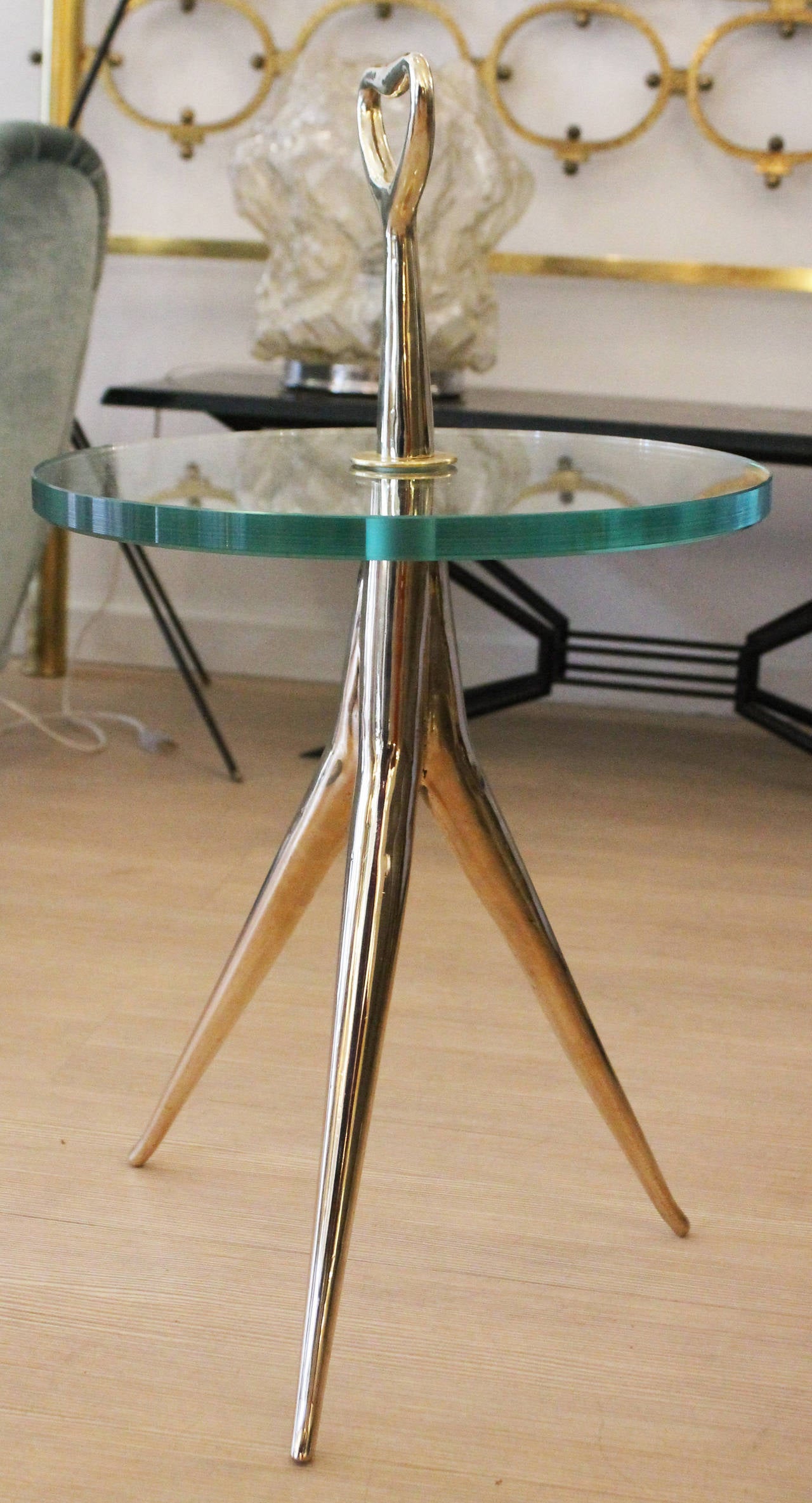 Elegant and sleek Italian bronze side table with three thin legs ending in a central body with handle. Thick circular clear glass at the center.
