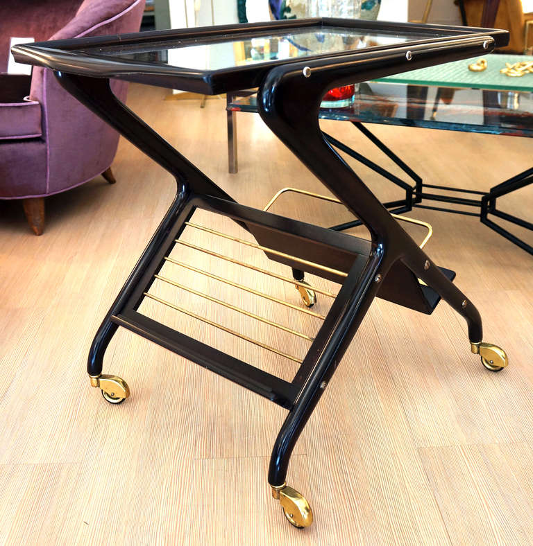 A great example of Italian 50's SCULPTURAL design. Reversed Y shaped legs sustain a protruding tray and bottles and magazine support on the lower part. Dark walnut finish. Polished brass elements. Rolls very well.