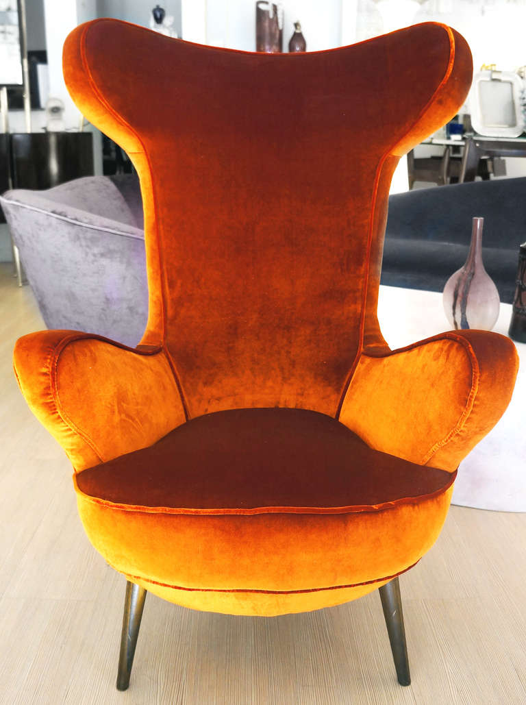 Unusual lounge chair made in Italy in the 1950s in the style of Carlo Mollino. It has a high back with rounded open wings, The armrests continue the same pattern. Elongated wood legs.