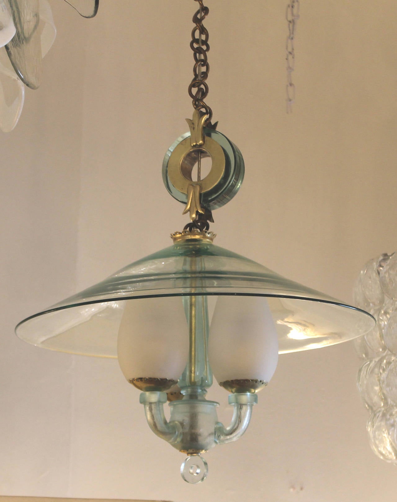 Elegant pendant made with a laguna green glass and brass details. The main section is composed of three glass arms holding small white frosted shades. This whole section is covered a by a larger laguna green glass shade. Holds three candelabra
