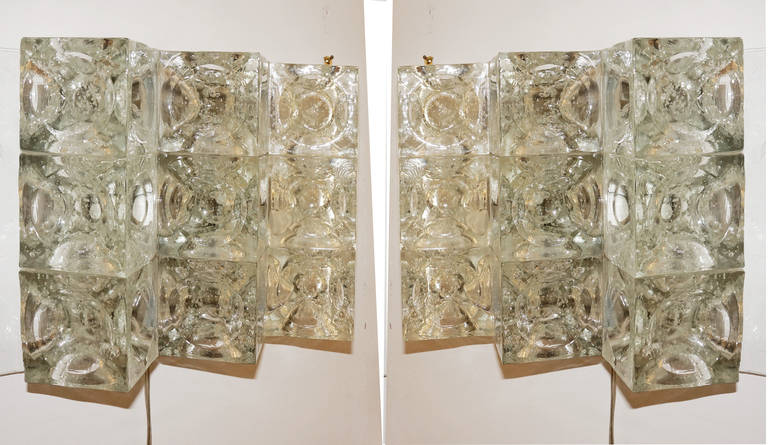 Each sconces is made with nine glass cubes with a spherical indent at the center. A metal structure mounts to the wall and to the top and bottom of the sconces.