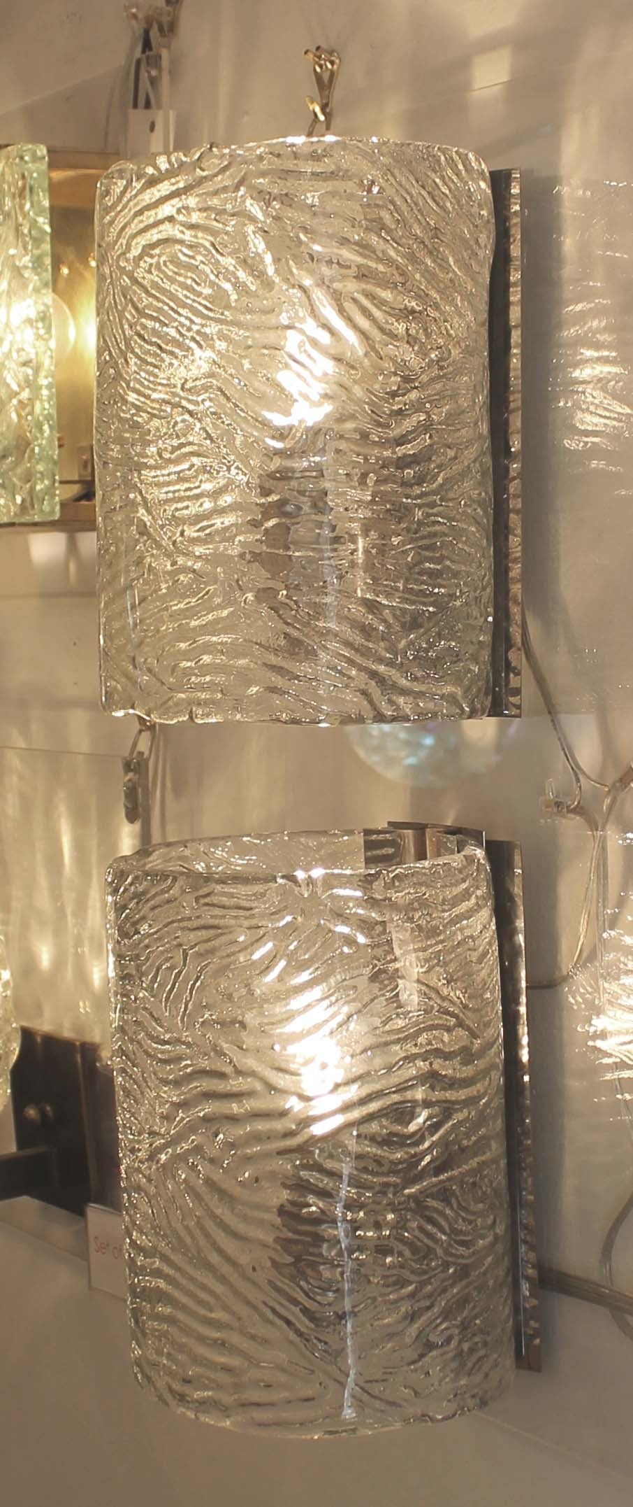 Pair of large cylindrical sconces featuring Murano handblown in a mold glass. The glass is clear and textured on the inside. The hardware is chrome and holds one regular E27 socket.
