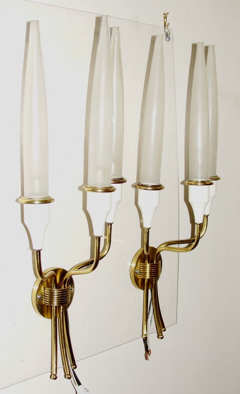 Sophisticated sconces with three brass arms ending in a white lacquered cup holding elongated glass shades. Quite unusual.
