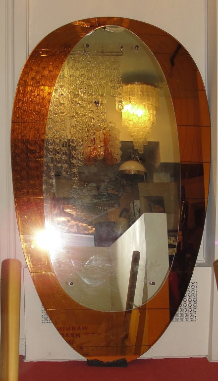Two egg shaped mirrors are superimposed. The gold  mirror that frames the regular mirror has horizontal as well as oval bevels excavated in the back side that give it.