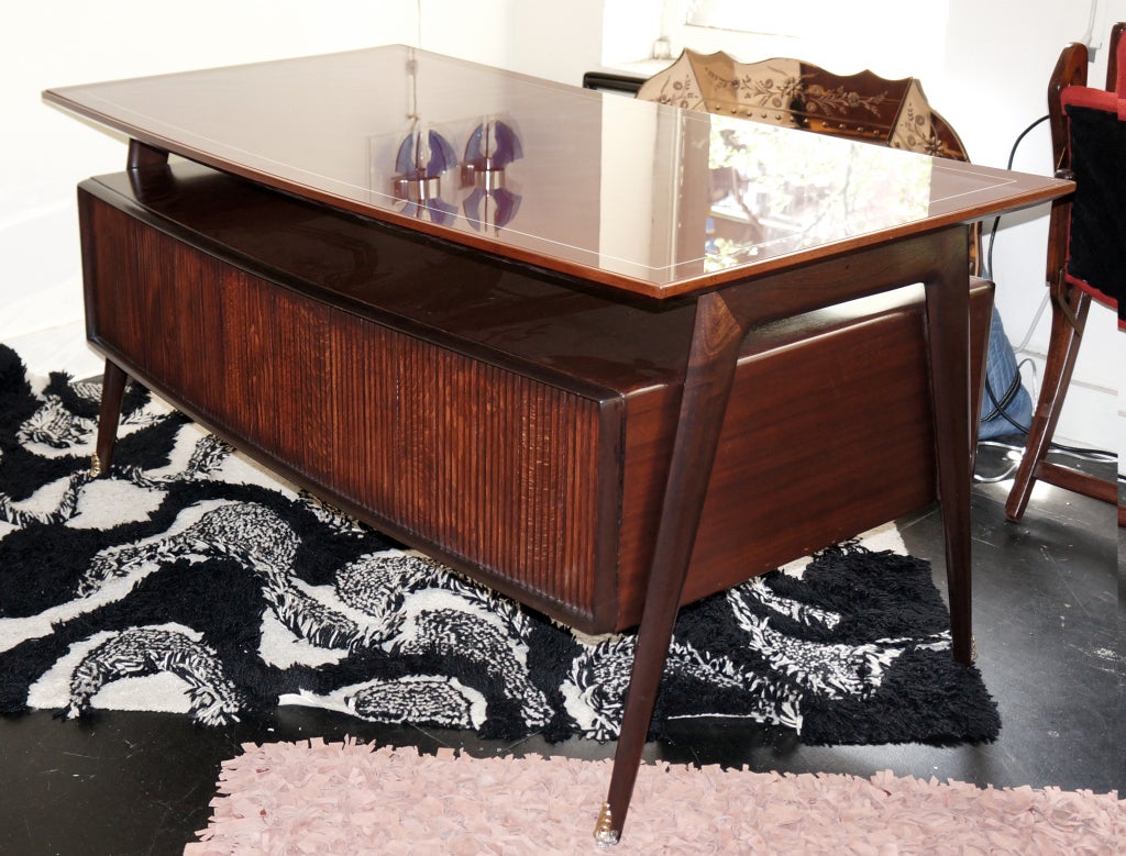 Posh 50's mohogany desk with elegant details. The front is made by a large framed paned carved in a way to create a series of parallel vertical lines. The back has six drawers paneled with two types of wood (mohogany and a light colored wood) making