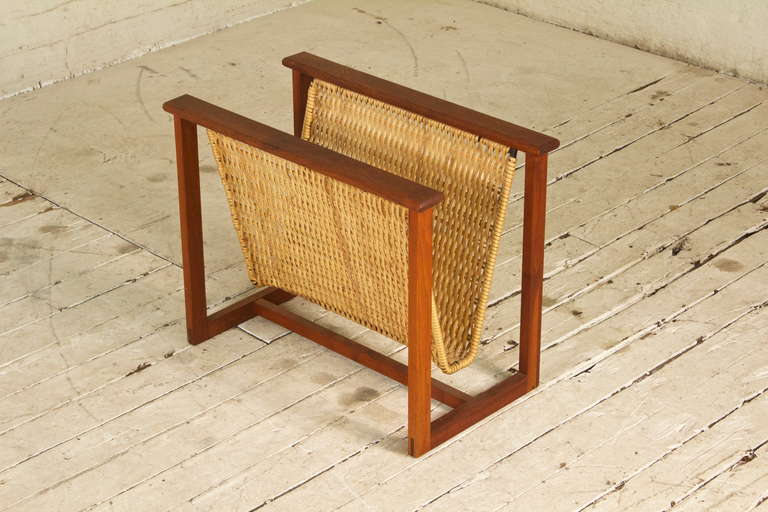 Handsome Danish magazine rack featuring a sturdy, joined teak wood frame, and a tightly-woven, plastic-laminated rattan basket. Simple yet sophisticated, this well-designed little piece is both functional and beautiful.