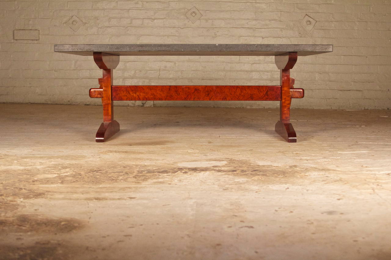 Unusual Arts & Crafts style coffee table with tinted Karelian birch trestle form base, and fossilized-black stone top. This table utilizes a wedged-tenon construction, making it completely demountable.