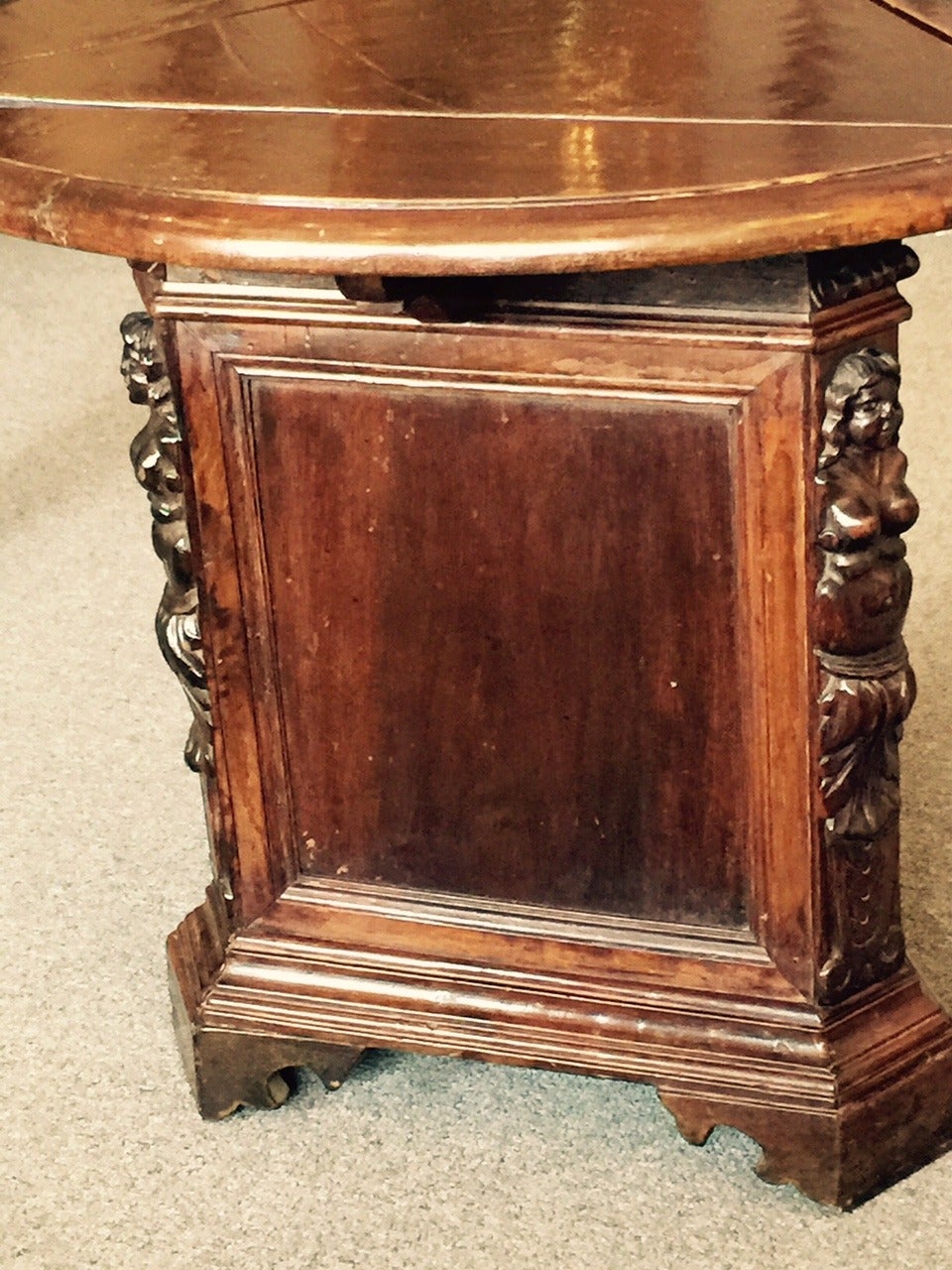 Interesting Italian walnut side table on a triangular stepped base. The three corners of the triangle are decorated with a carved figure of a woman in the classical style. A door in the base opens to allow storage with one shelf. The top is circular