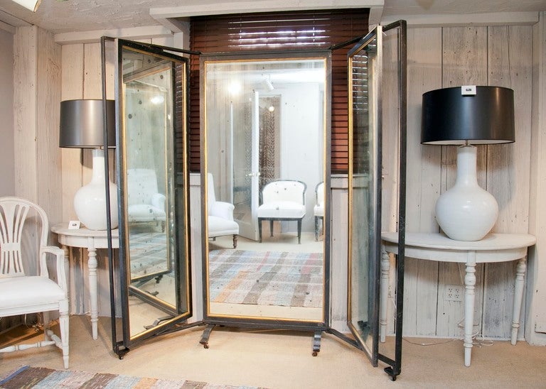 Gargantuan tri-fold salon-style mirror with rotating side panels, black iron framework, gilt fillet and original antique glass as well as casters.  The perfect statement piece for the dressing room, master bedroom, entry or wherever a full-length