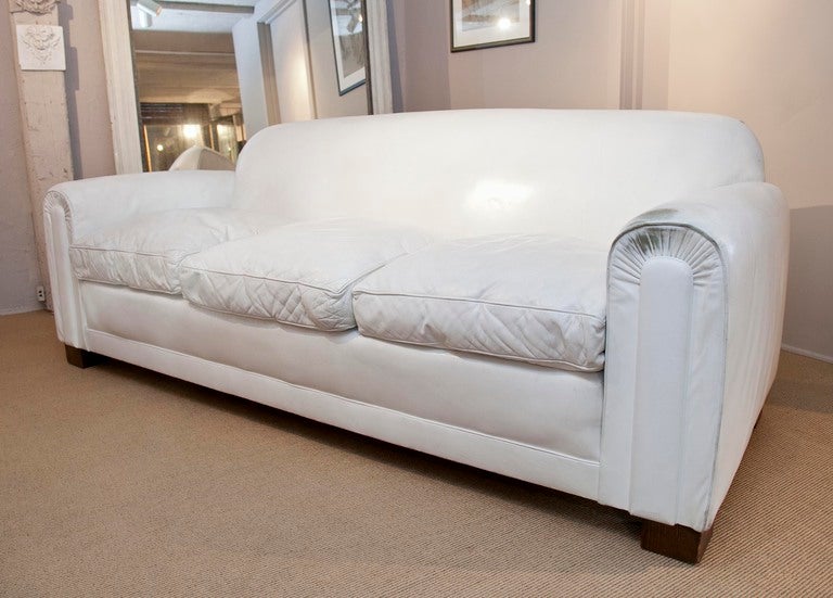 Very comfortable deco-style sofa in original white leather raised on block wood feet in the style of Jean-Michel Frank.  Great presence and form.  Matching pair of club chairs listed separately.