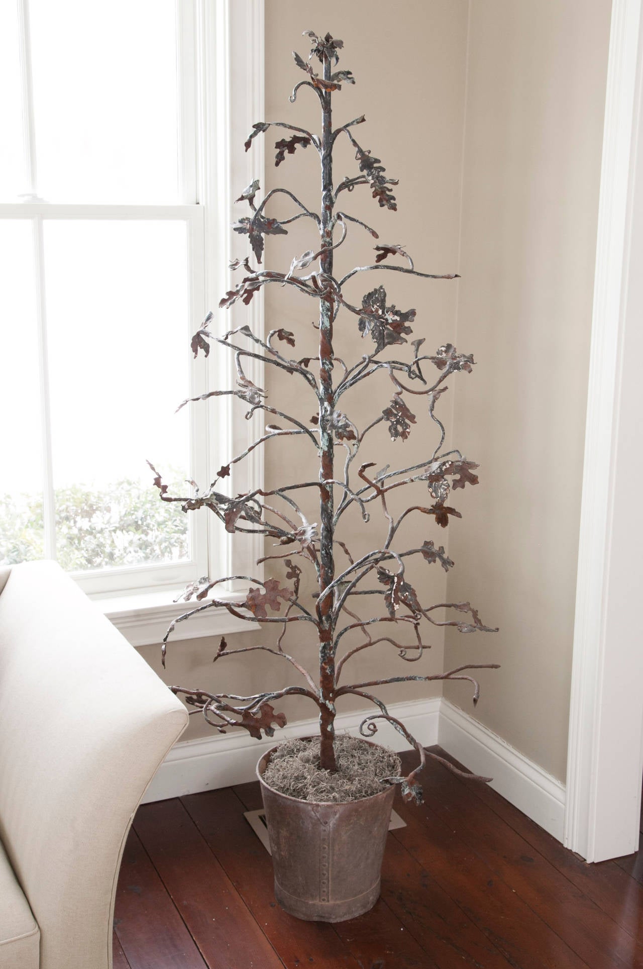 Iron tree with trunk emerging from a galvanized metal pot weighted with concrete. Features tole branches and foliage. Wonderful crusty and rusty patina with age-related paint loss.