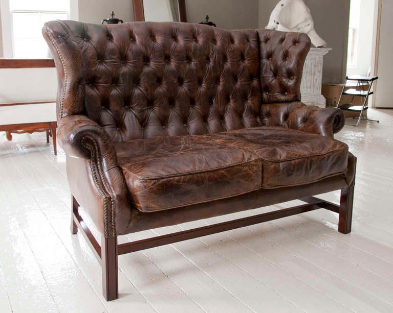 George III style tufted wing-back leather settee on squared front legs with stretcher.  Leather has aged gracefully with wonderful patina.