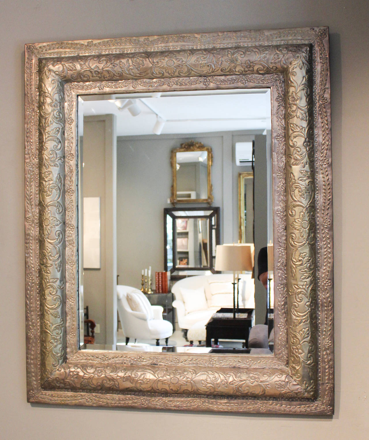 Intricately hand tooled and etched tin frame with floral and scroll motif encasing beveled mirrored glass.