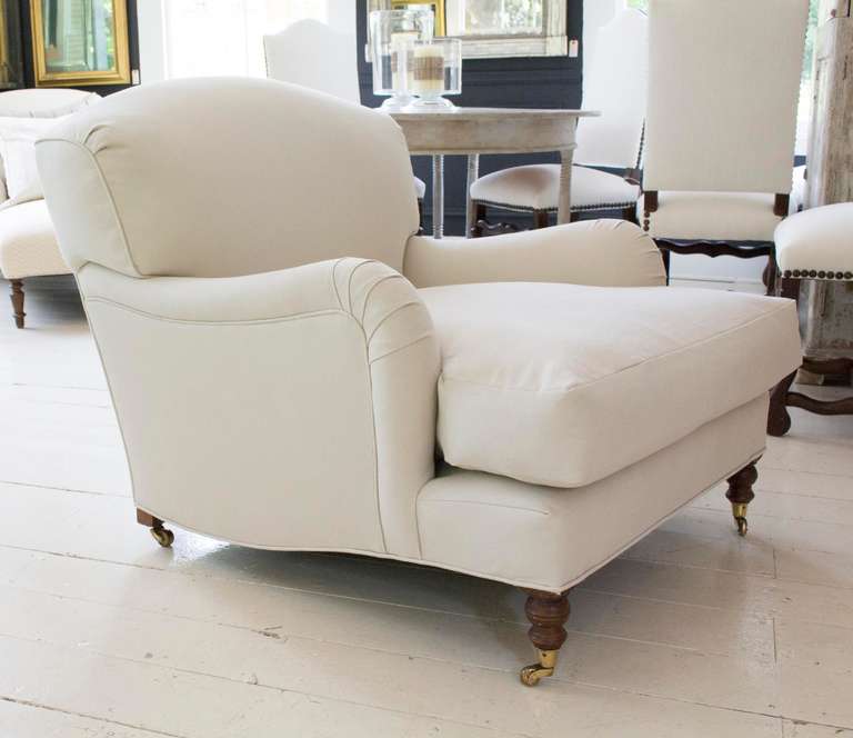 The pair of deep, comfortable custom-built George Sherlock club chairs has beech frames; hand-sprung back and seat fitted with fixed back cushions and loose seat cushions and are raised on turned legs with brass castors. Newly upholstered in Rogers