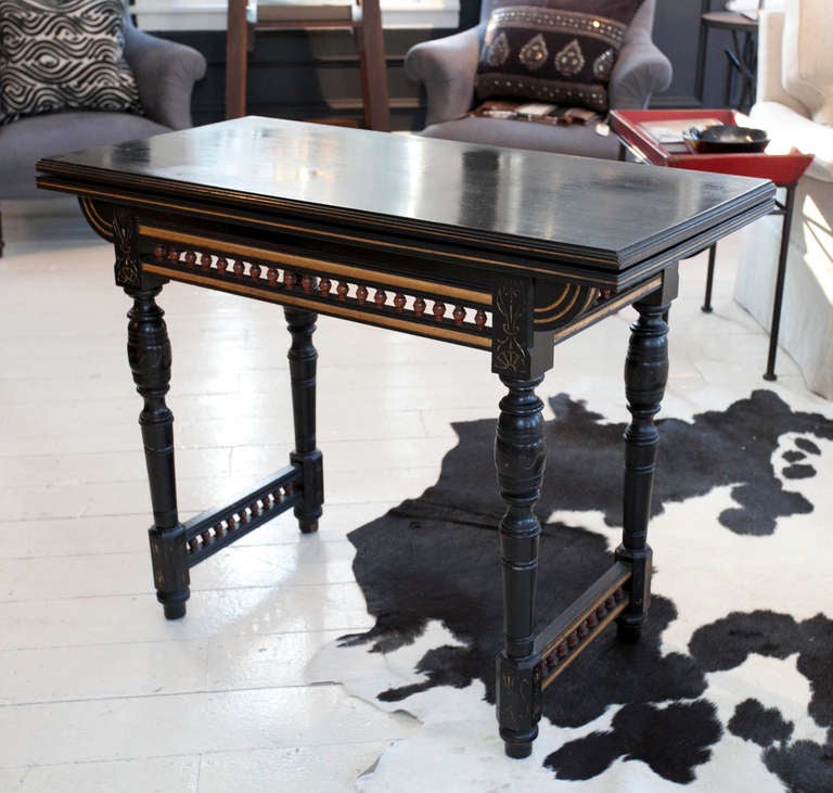 Ebonized Eastlake game table with turned legs, gilt detail and wood stool-like spacers.  Top flips open to become a game table covered in blue felt.  Stamped R. Crosby, Liverpool.