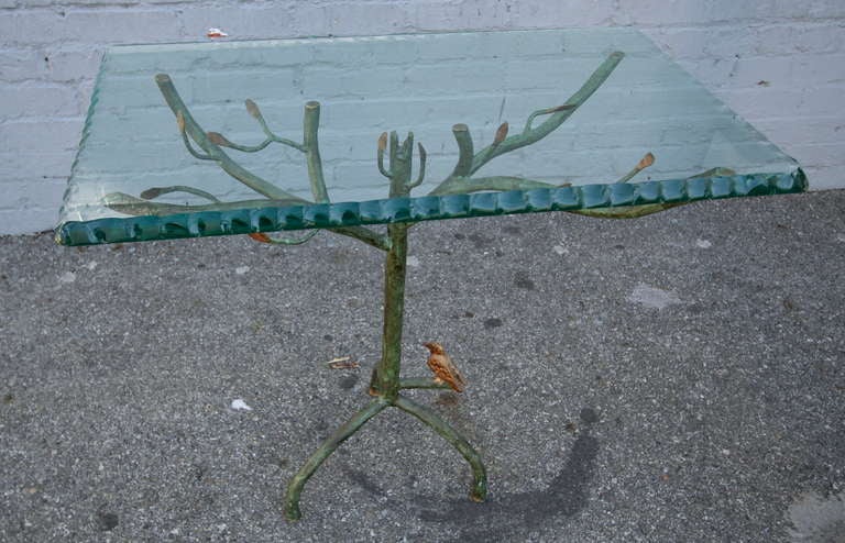 Table d'appoint sculpturale avec base en métal en forme de branche d'arbre avec des feuilles dorées et un oiseau.  Le plateau en verre a un bord décoratif.