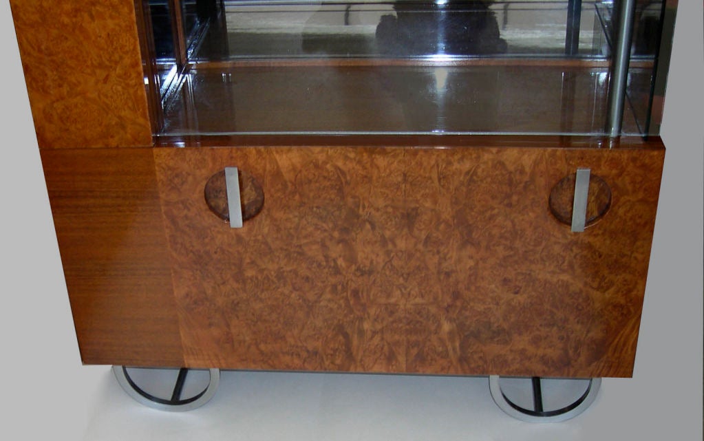 This incredible cabinet was designed by Gilbert Rohde for Herman Millet in 1933. It is a combination of walnut and walnut burl with satin chrome base and  pulls. Te inside of the display area is lined with the original black mirror. The bottom