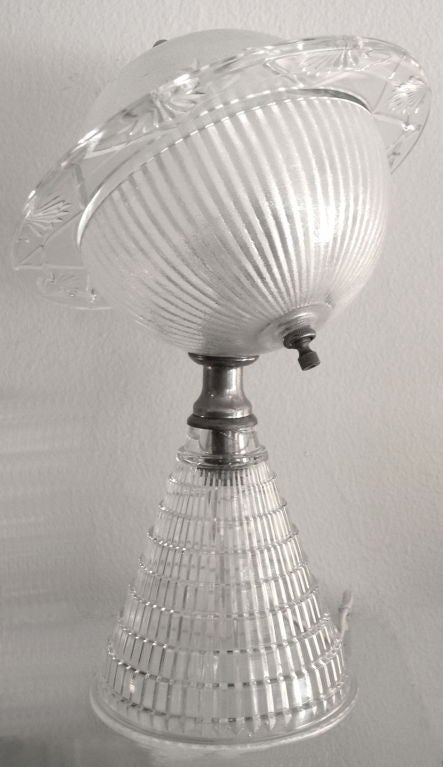 This rare lamp was made in the 1930's. It is made of clear glass with star and planet designs molded into the top section of the lamp and ridged layers on the base. The top lifts off to change the bulb.