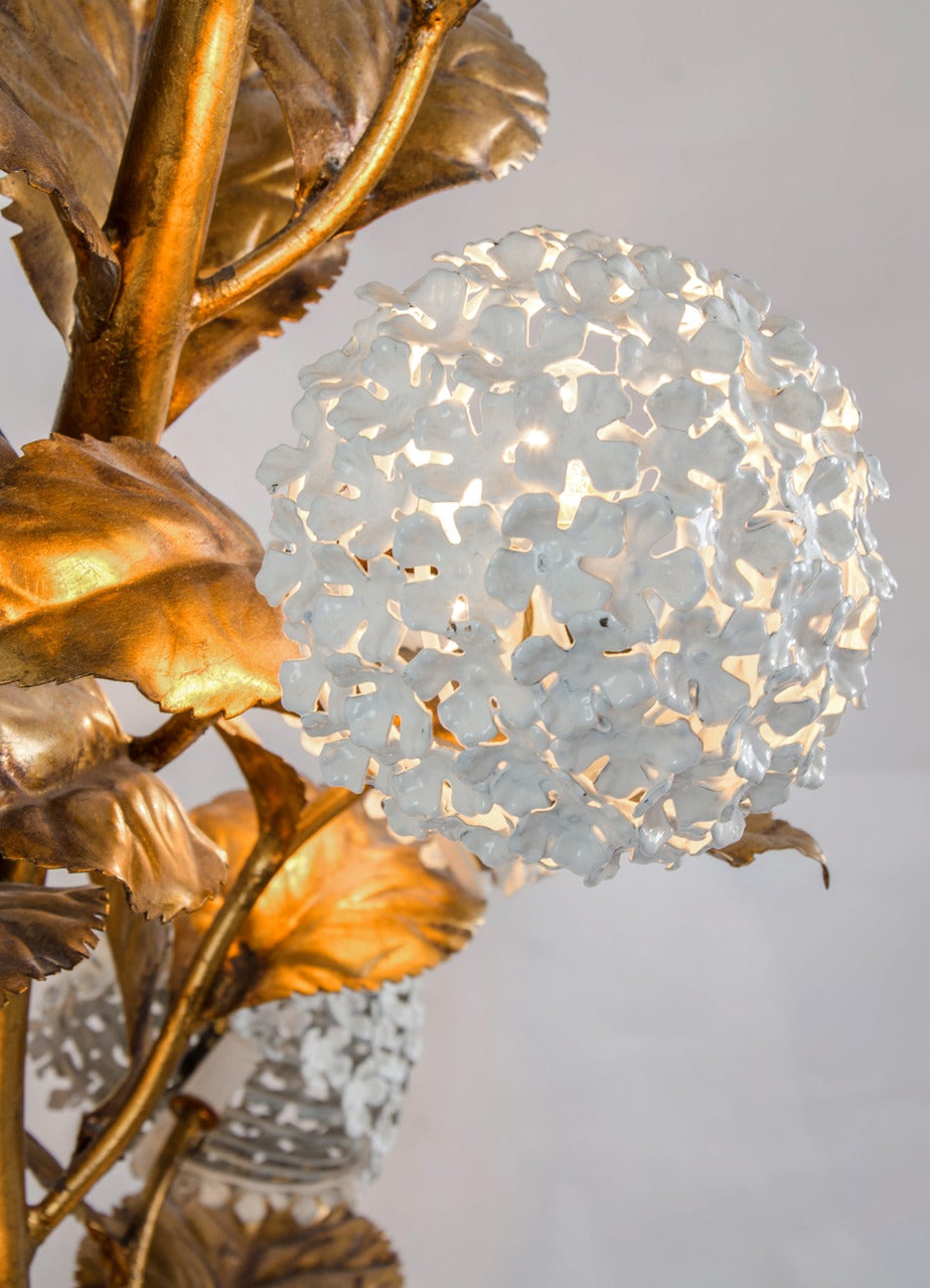 Rare American 1950s standard lamp of gilded brass with white enamel hydrangeas growing from an ornate flower pot. An abundance of leaves with  eight flower in full bloom, each giving a glamorous diffused light
Matching table lamp and wall light