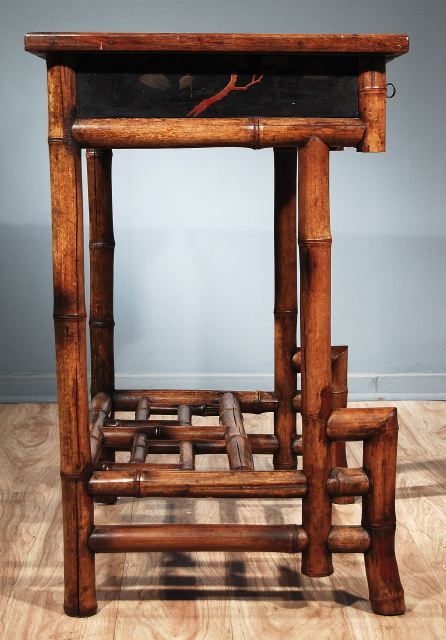 The rectangular top with an inset red leather writing surface within black lacquer borders, above three short drawers, raised on bamboo legs joined by a fretwork stretcher.