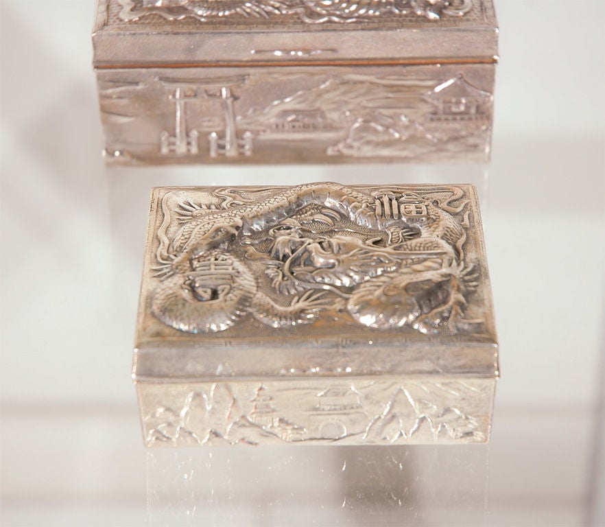 Four Japanese silverplated boxes. Hexagonal box depicts elephants crossing a bridge. The cigar holder has an aesthetic theme of fishes, sea shells and seaweed. The two rectangular boxes are decorated with dragons. Please note that the price is for