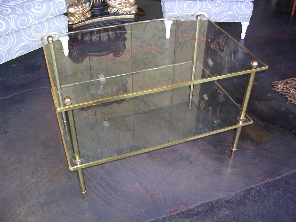 A functional two level brass table. Brass legs are inset into the glass shelves.