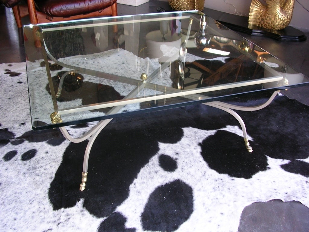A Hollywood Regency ram's head coffee table in brushed nickel and gilded bronze. Decorated with hoofed feet and an acorn finial in the center of the X. Glass measures 46