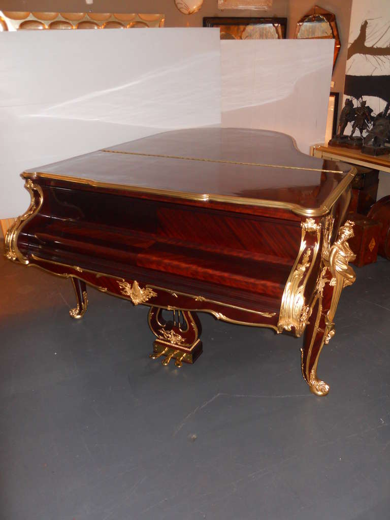 Astonishing Steinway Mahagony Piano, gilt bronze mounted core decorated with foliate scrolling encadrements (frame) and having stylized dolphin and pierced foliate mounts, the cabriole legs headed by figures of Figaro and Rosina. New gold plated in