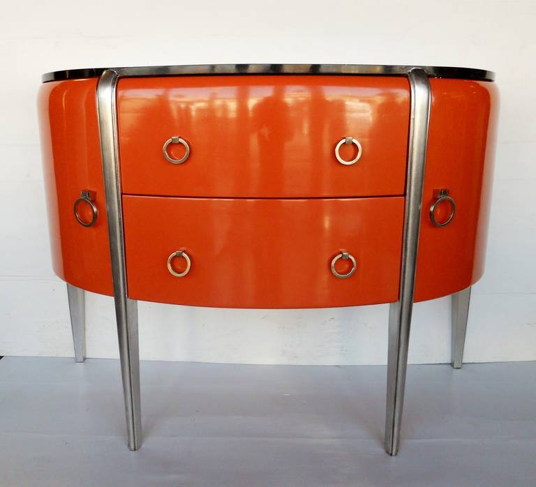 A stunningly elegant pair of Art Deco commodes in the style of Michel Dufet. Commodes are in burnt orange lacquer with silver leaf legs, brushed nickel handles and faux marble tops.
