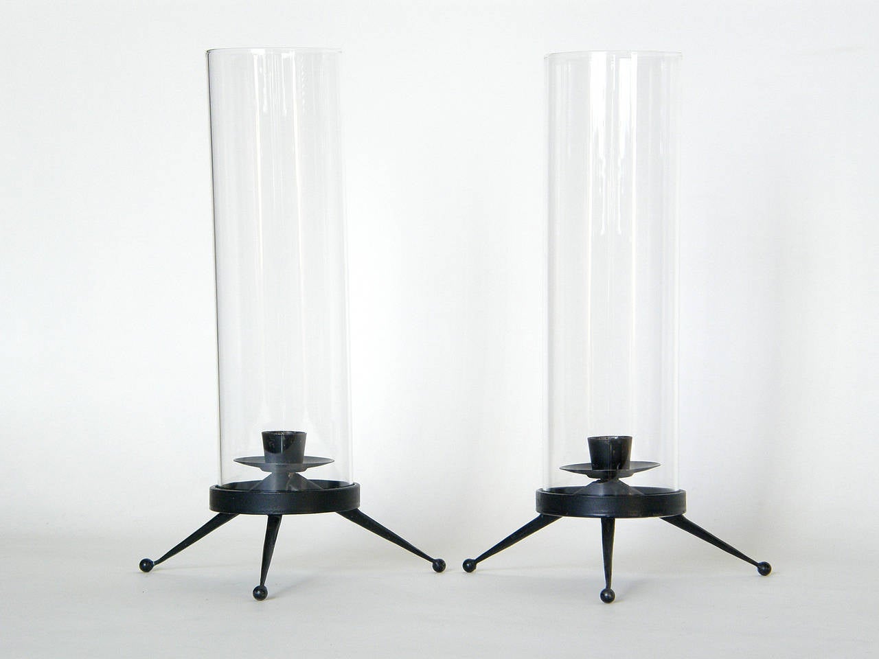 Pair of iron tripod candleholders with glass hurricane shades from the  Candelabra Group designed by Tony Paul and manufactured by Woodlin-Hall.

Please contact us if you have any questions.