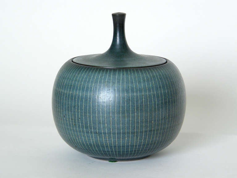 Lidded ceramic jar by California potter Harrison Mcintosh. The simple form combines a restrained elegance with an organic quality. The finely incised vertical lines resemble the natural decoration found on some varieties of gourds. The refinement of