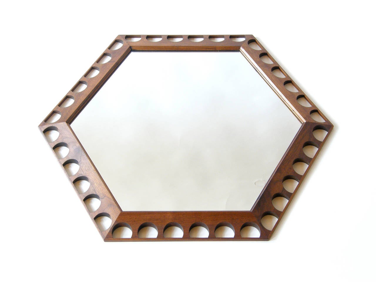 Hexagonal wall mirror designed by George Nelson and made by Howard Miller. The walnut frame is beveled and pierced by semi-circular shapes.

The measurements given correspond to the orientation of the mirror in photo #2. The hanging wire is set