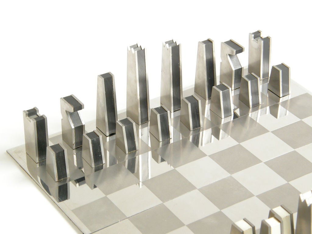 Cut steel chess set with interlocking 2 piece steel board. The precisely cut, sculptural pieces are made of black and white plastic laminated between sheets of stainless steel. This chess set is a nice example of the chic, masculine industrial