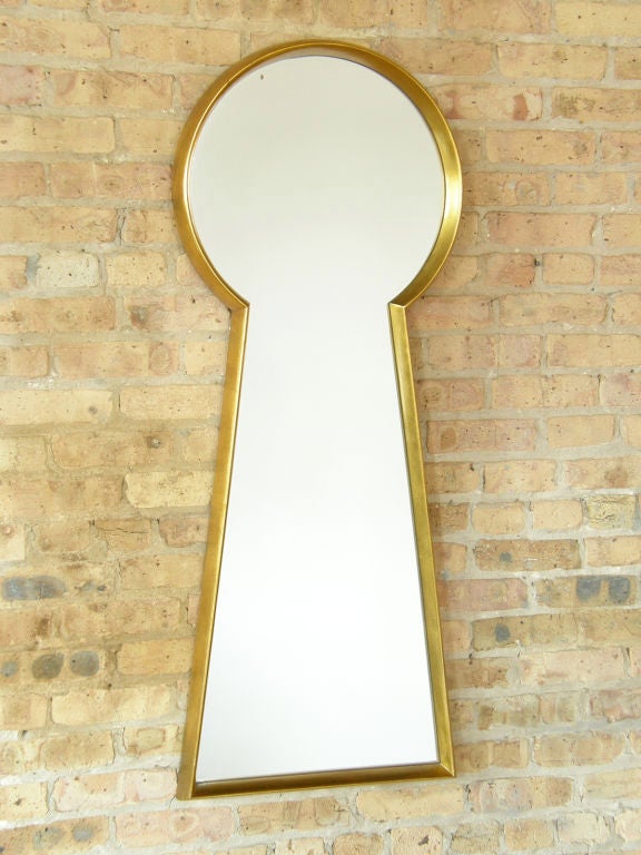 This whimsical mirror in the shape of a keyhole has a deep gilt wood frame.