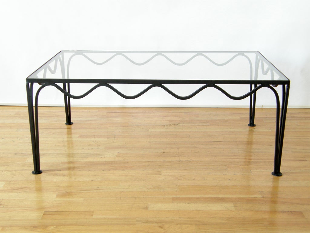 Coffee table with playful squiggling iron frame and glass top. Frame is made from solid stock. Glass sits down in the frame.