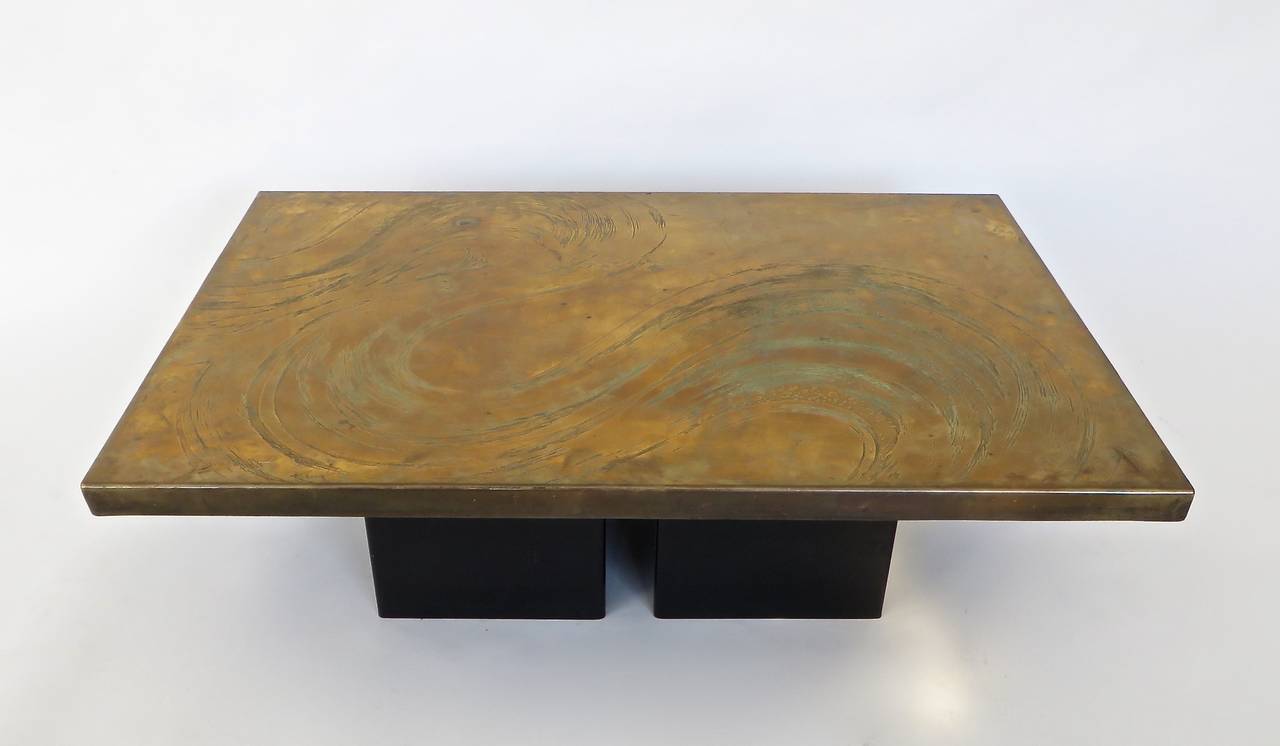 A Belgian etched brass coffee table on two black enameled metal pedestals. The pattern is like a wave or cloud with varying deeply etched lines and drops and differing colors of brass and copper patina. Varying original patinas and age appropriate