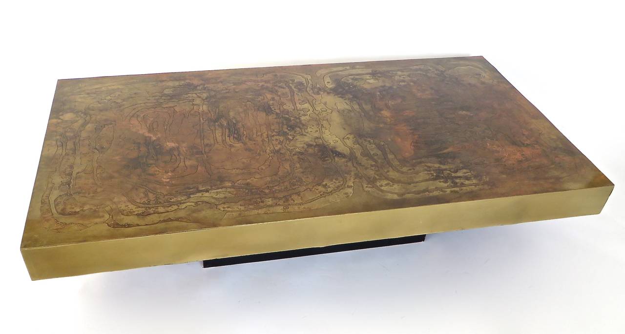 A large etched abstract scene Belgian signed coffee table on a black laminate base. The undulating abstract design in both copper and varying shades of darkened brass patina with raised areas. Smooth brass sides. Signed although the signature a bit