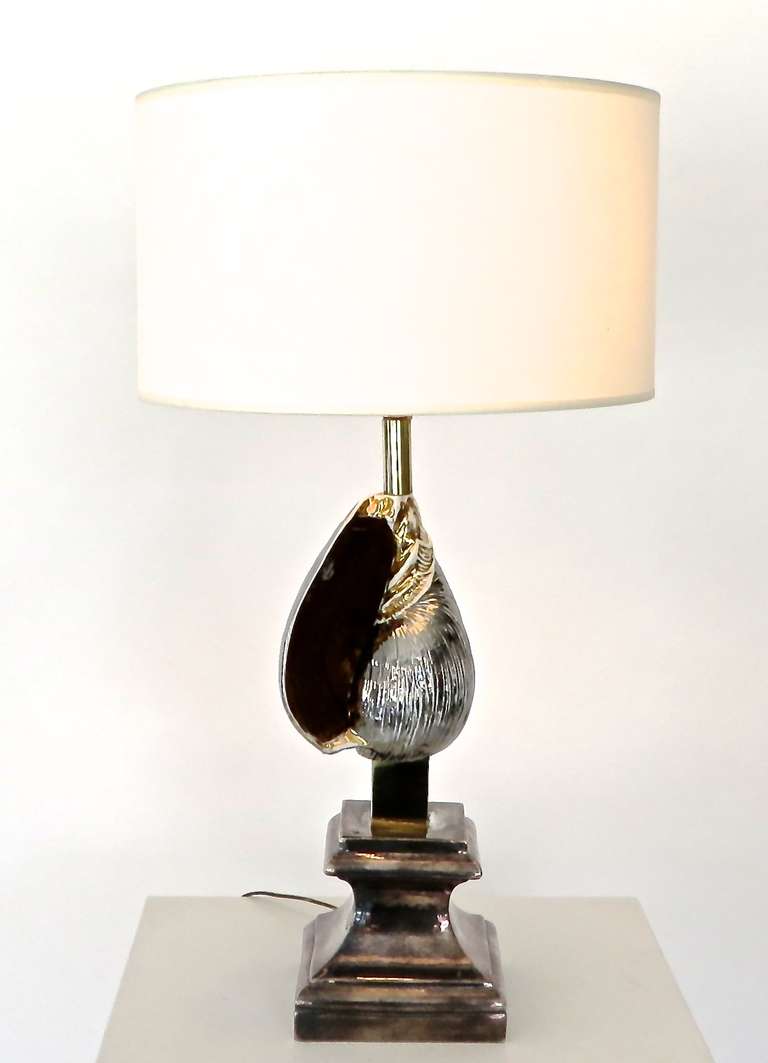 A French table tamp with silver and gold glazed accent ceramic seashell on a classical pediment. Brass accents between the base and the pole of the lamp.
French, circa 1970. The base has a beautiful patina but could also be brought to a high polish.