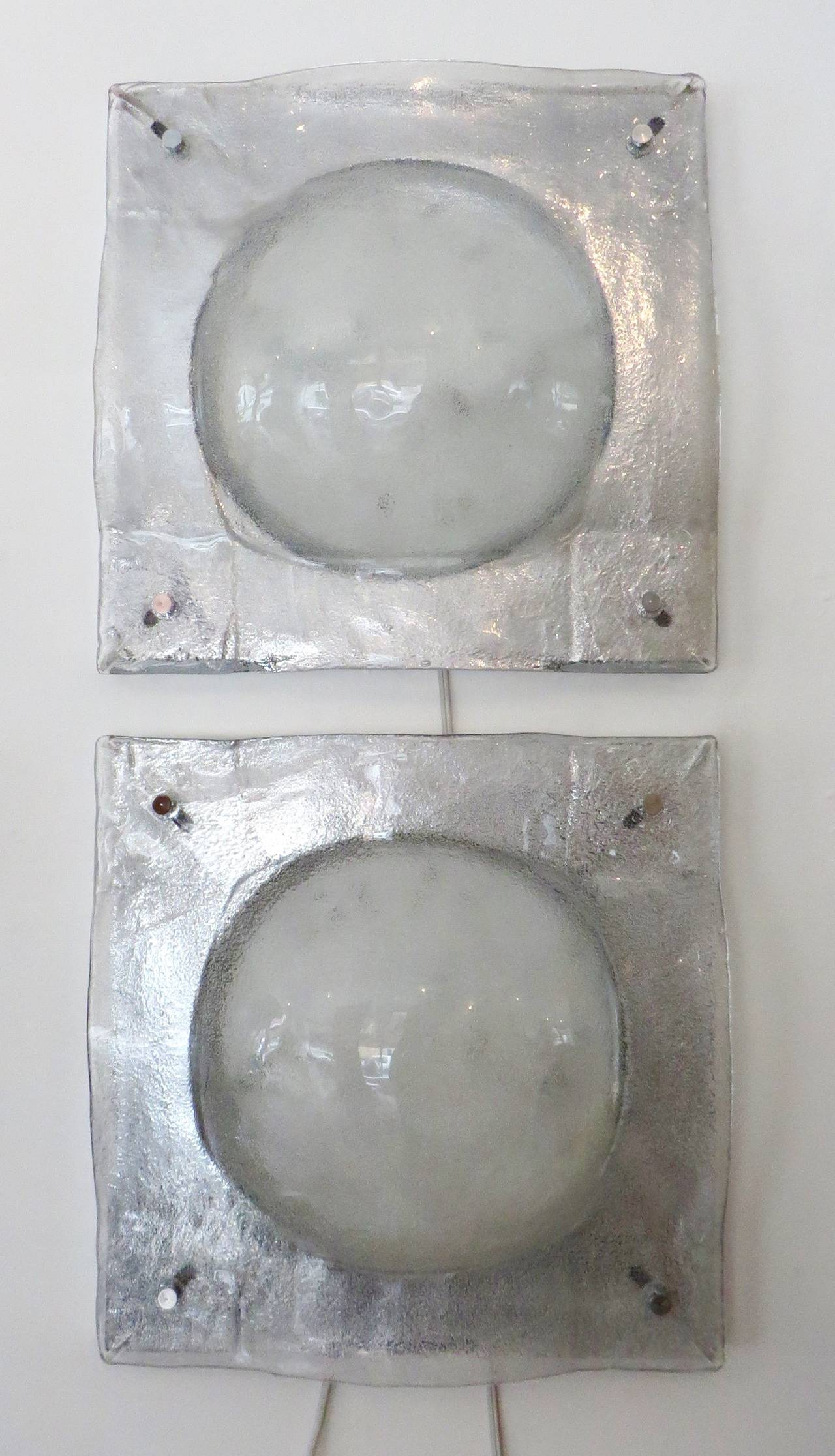 These Italian cast glass sconces by Mazzega have very silvery gray color especially with the chromed steel frames they attach to providing a silvery background. 
Each sconce has two sockets and can take up to 40 w each socket. 
A very impressive