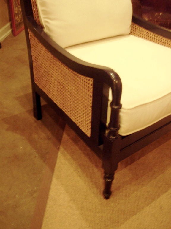 One pair of British Colonial style club chairs. Ebonized frame with cane work, covered in white canvas.