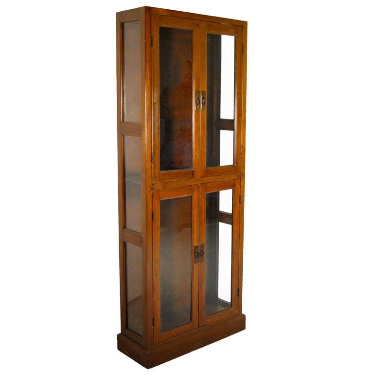 A tall glass front display cabinet from Tianjin, China c.1900. This beautiful cabinet is made from brown teak wood and has four glass paneled doors with brass pulls.